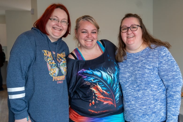 Three people stand together inside a home, smiling.