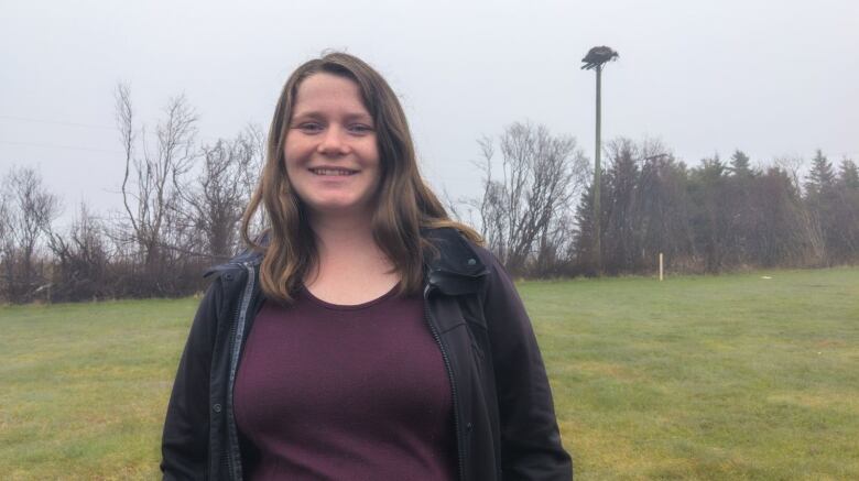 A woman stands with an osprey platform behind her