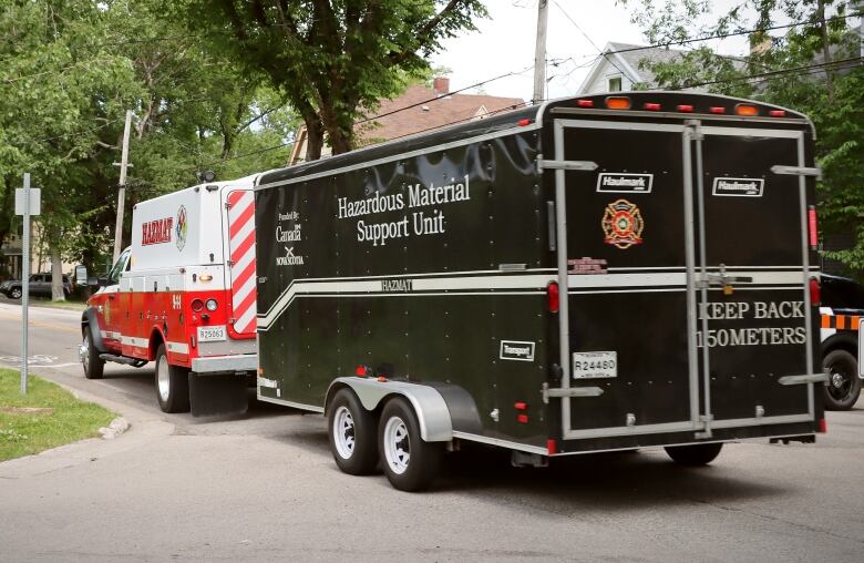 A red and white fire truck marked Hazmat pulls a black trailer marked Hazardous Material Support Unit down a street.