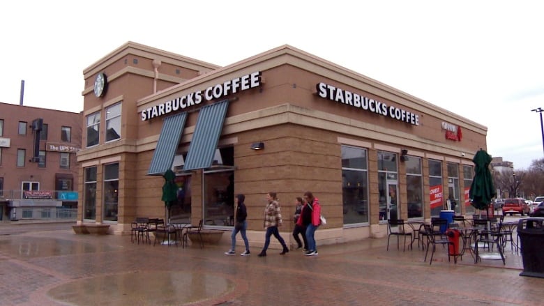 People walk past a store with a Starbucks sign in a city neighbourhood.