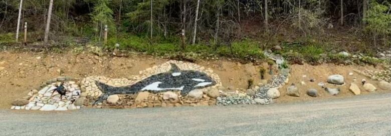 A photo of black and white orca artwork made using rocks. 