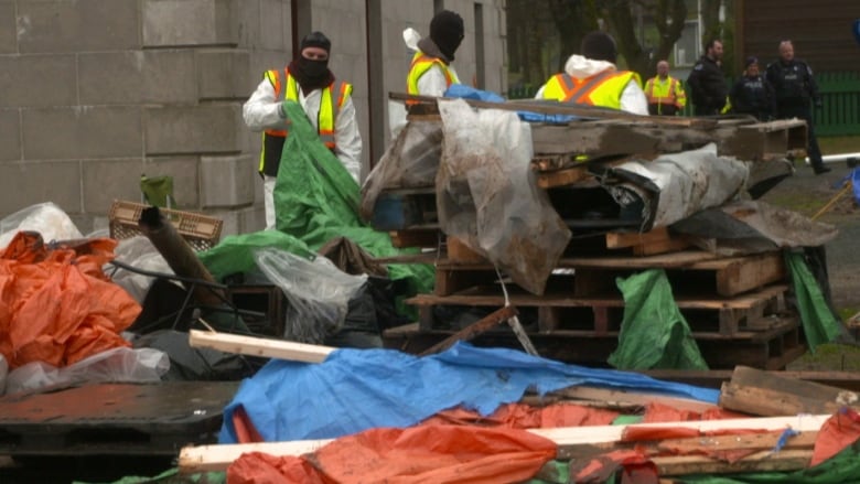 People in white hazmat suits clean up piles of wood plastic and trash.