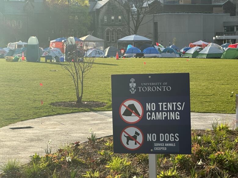 A sign that reads no dogs or tents and camping on University of Toronto property. In the background, tents can be seen.