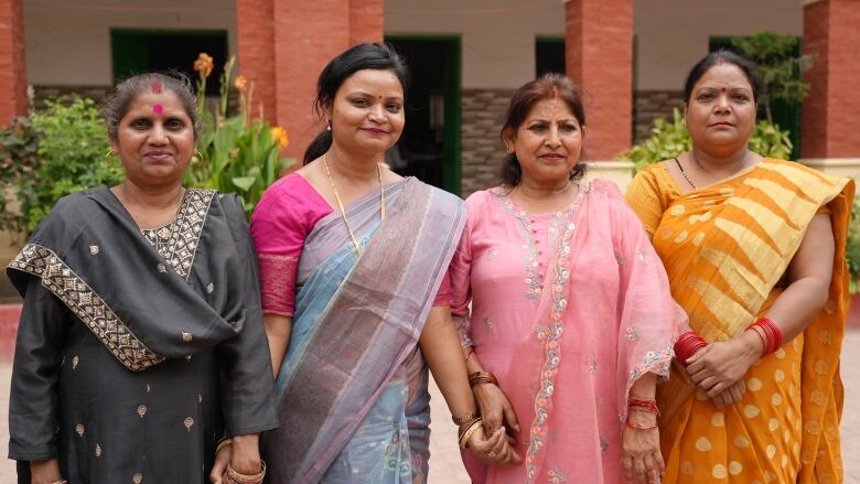 Four women in saris hold hands and look at the camera.