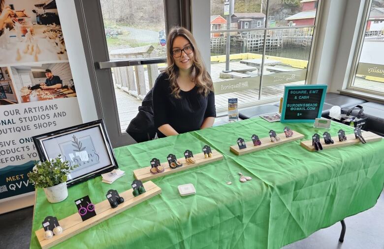 Woman with blonde hair wearing a black shirt sitting behind a table that has various earrings for sale.