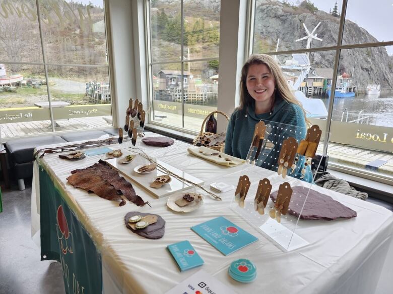 Woman with light brown hair sits behind a table with her crafts - earrings and leather she tanned. 