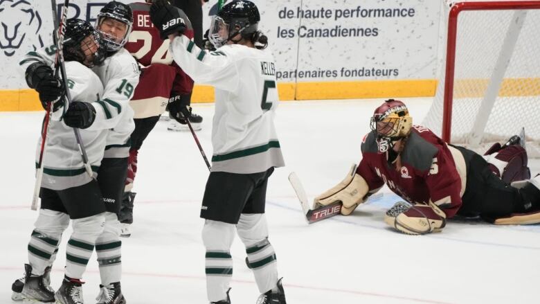 Three female hockey players are seen celebrating a goal as the opposition goaltender is seen laying on the ice.