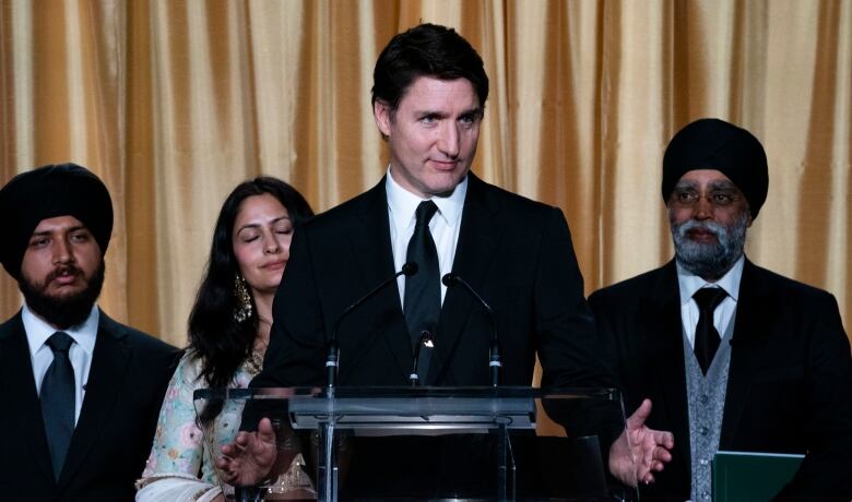 A person speaks at a lectern as other watch on behind the speaker.