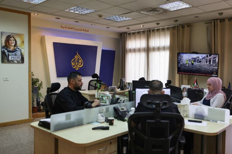 Three people sit at desks in front of computers in an office.