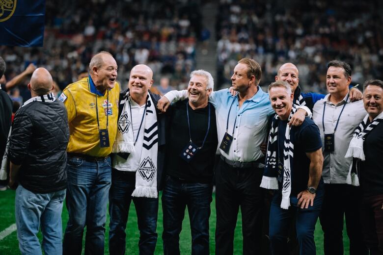 A group of old men share a laugh on a football pitch.