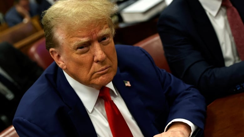 Donald Trump, frowning and hunched over in a courtroom, looking up at the camera 