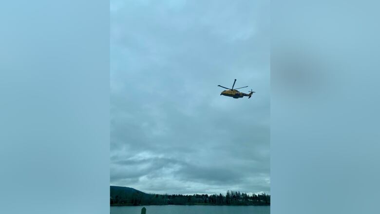 A helicopter flies above a body of water in a grey sky.