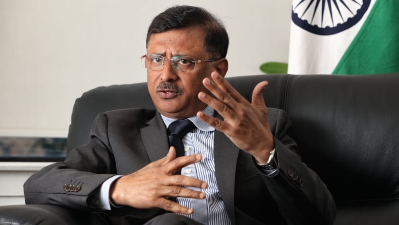 Sanjay Kumar Verma, a man in his 50s is pictured sitting in a chair wearing a grey suit gesturing with his hands as he speaks