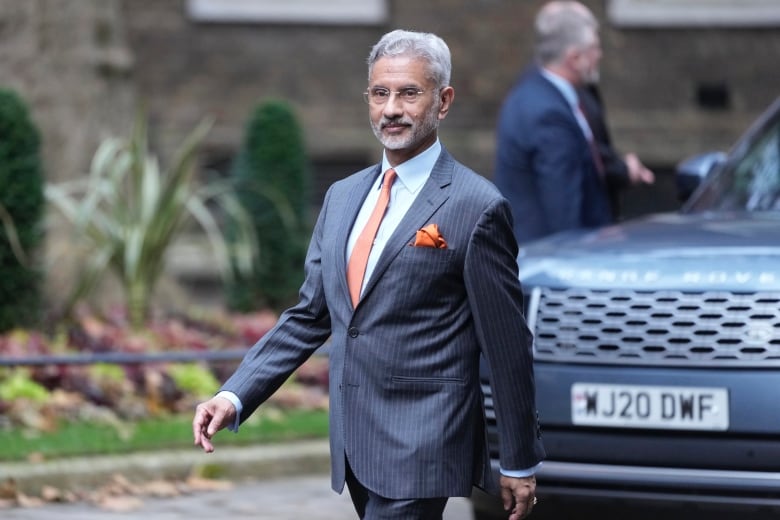 Indian minister of external affairs Subrahmanyam Jaishankar, shown with grey hair, glasses, wearing a dark suit with an orange tie walks outside. 