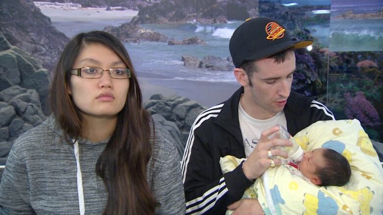 A woman sitting next to a man feeding a newborn with a bottle.