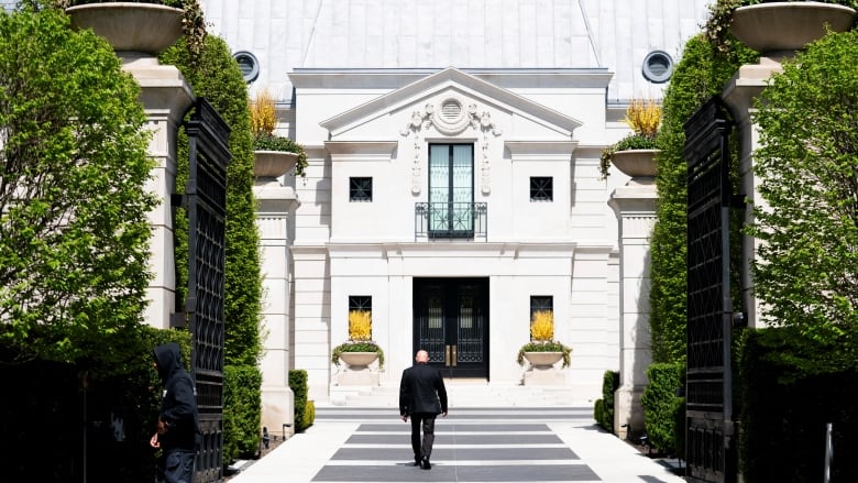 Photograph showing a man walking towards a large white mansion. 