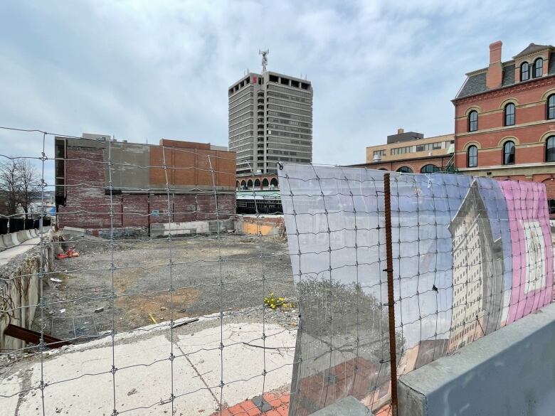 A photo of a derelict site on a city street surrounded by wire fencing.