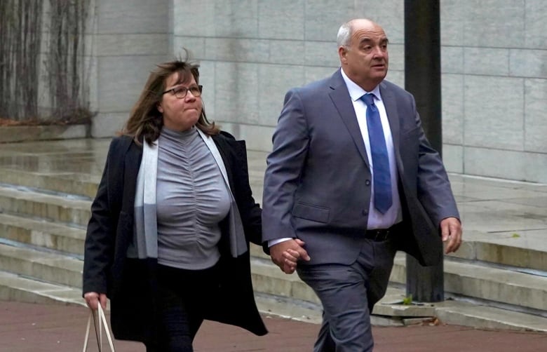 A man and a woman hold hands as they walk outside on a cloudy day.