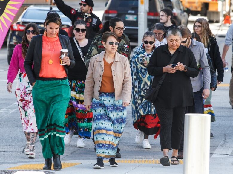 A group of people walk together,  many wearing ribbon skirts.