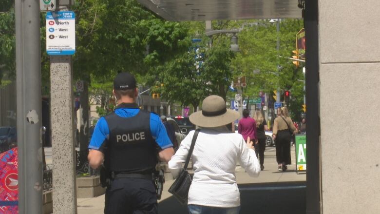 A police officer walks alongside a senior citizen on a city street.