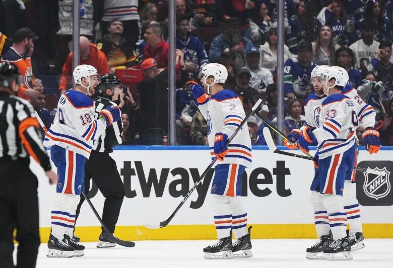 Hockey players wearing white celebrate on the ice.