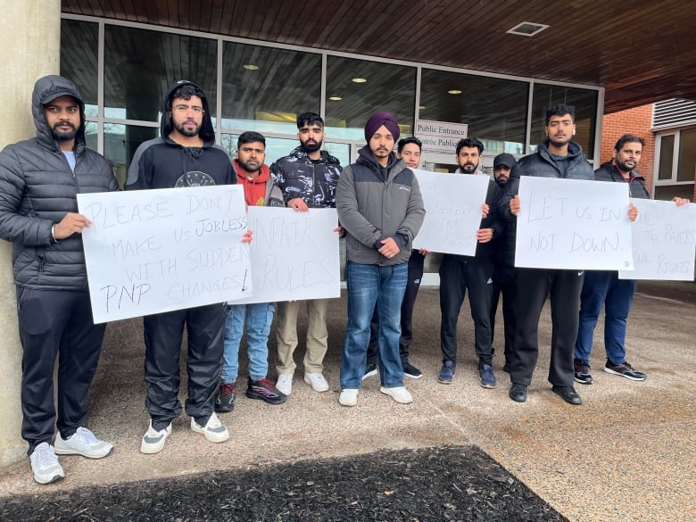 A group of about a dozen men and women hold signs outside a building.