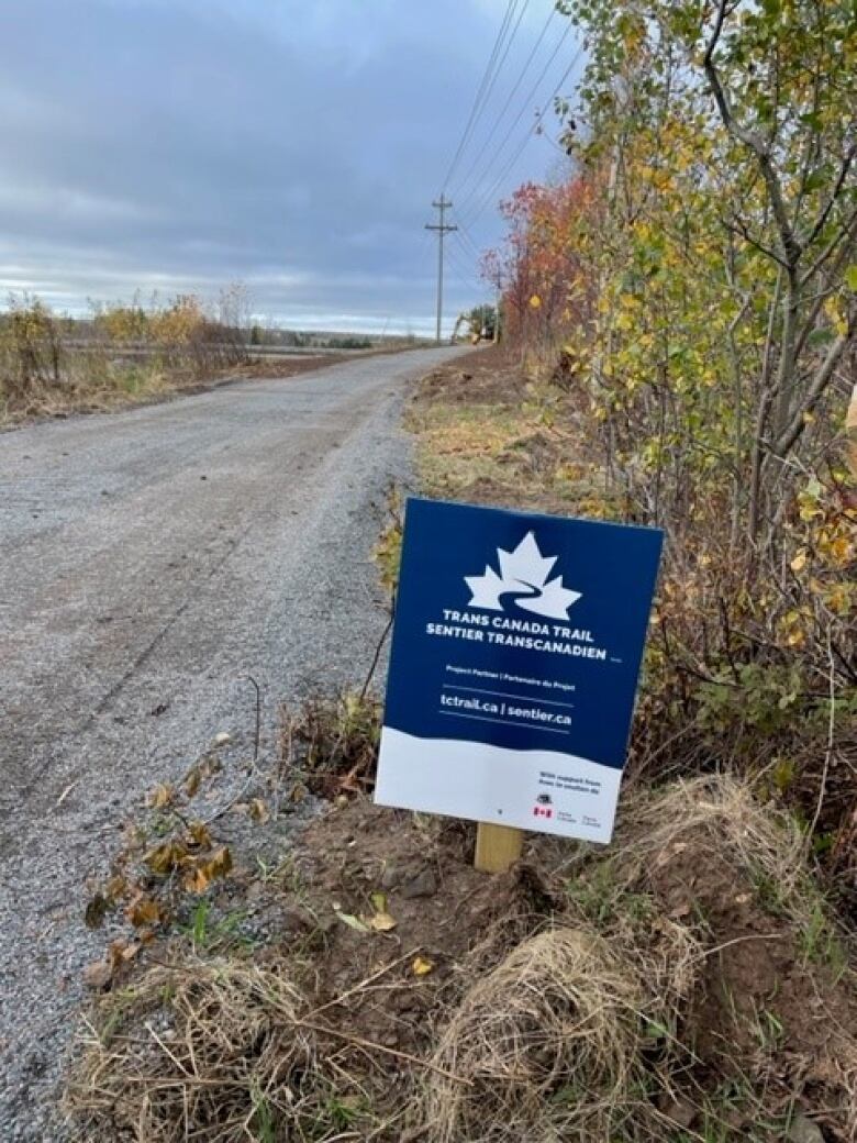 A blue and white sign on a stake next to a rail bed.