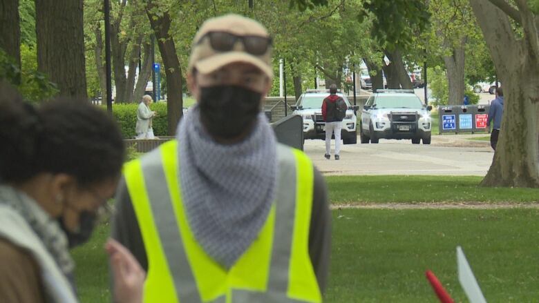 A person in a high-visibility vest with campus police in the background