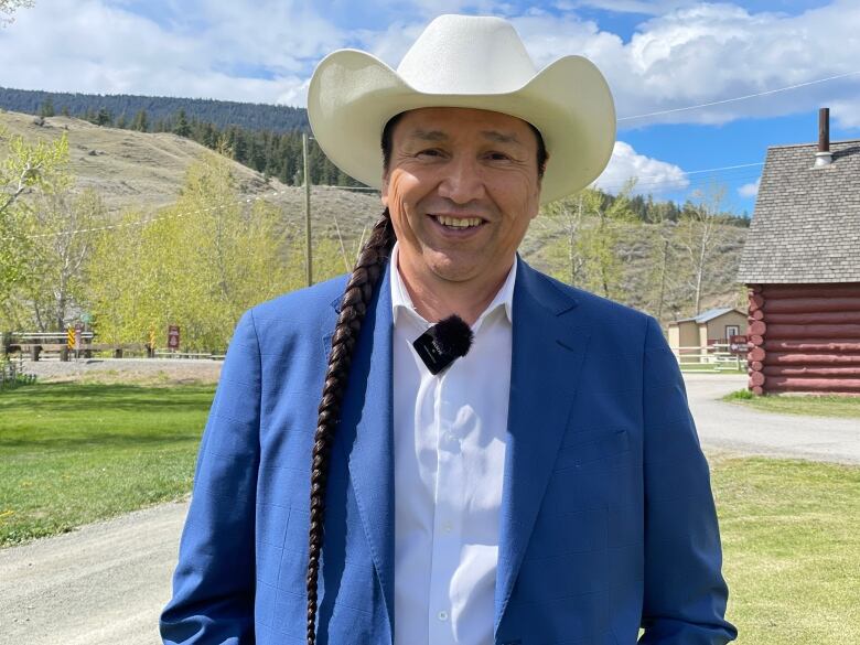 Man in a cowbow hat with blue jacket stand in front of log buildings