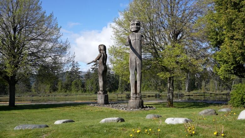 Two wooden carved figures, one man and a woman, standing with their arms outstretched. 