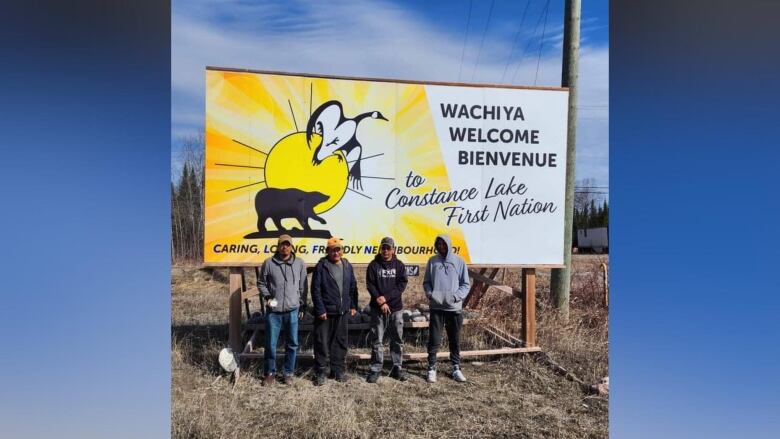 Four people stand outside in front of a welcome sign.