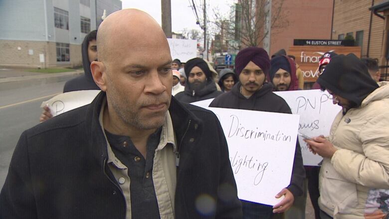 A man speaks in front of a group of protesters with signs.