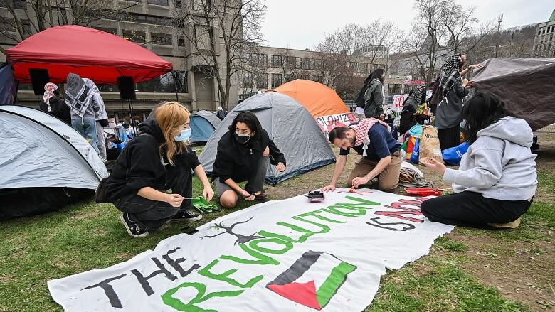 People work on a sign during a pro-Palestinian demonstration at an encampment at McGill University in Montreal, Saturday, April 27, 2024.