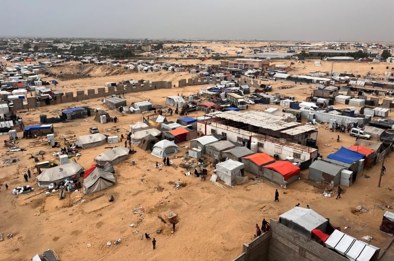 An aerial photo shows people preparing to leave a tent camp. Hundreds of tents are visible.