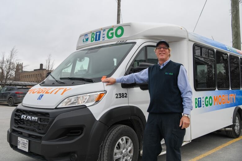 A driver leans against a mobility bus designed for transit users with additional mobility needs.