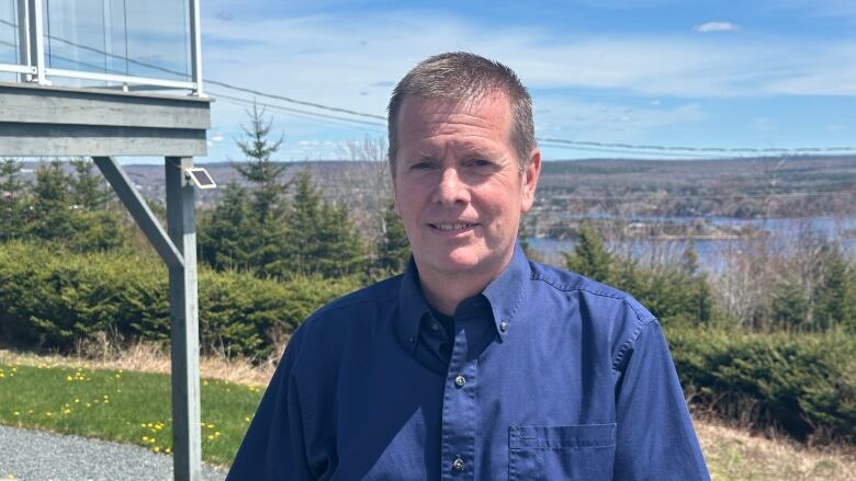 a man smiles for a portrait in front of a deck and ocean view. 