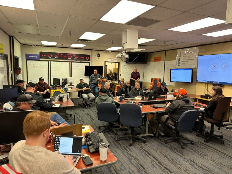 A group of people sit at desks in a crowded room. 