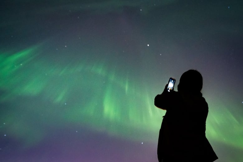 A person takes a picture of northern lights above them.