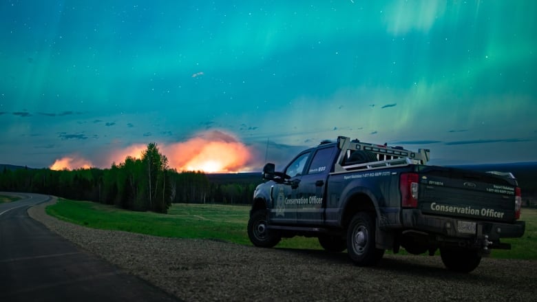 Plumes of smoke arise from a fire with the northern lights just above it.