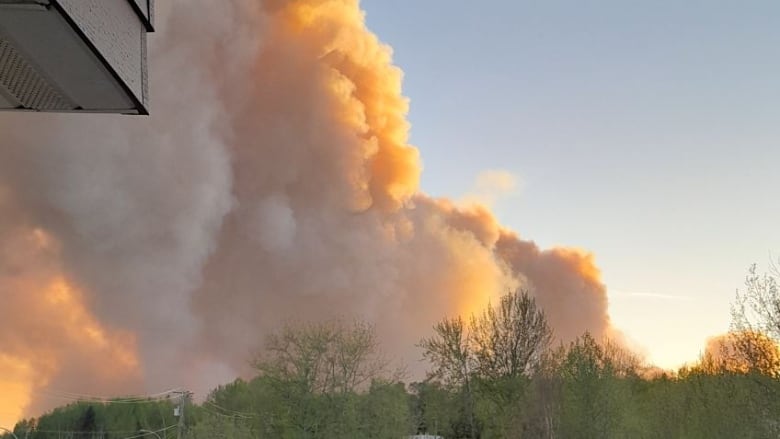 Large plumes of orange smoke are seen behind a row of houses.