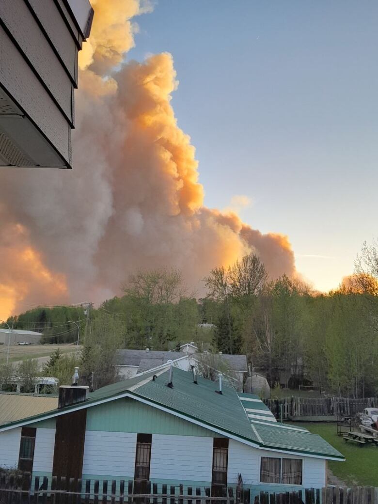 Large plumes of orange smoke are seen behind a row of houses.