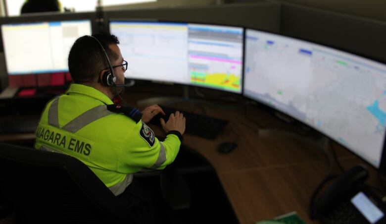 A man with a yellow Niagara EMS shirt on looks at computers. 