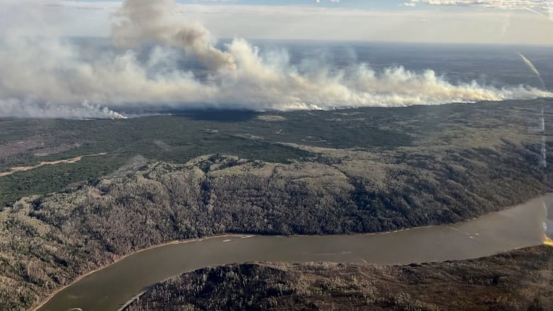 An aerial image of a wildfire burning near a river. Smoke fills the sky. 