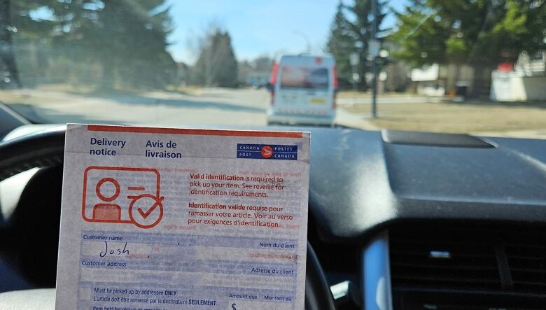 This photo was taken from inside Josh Kralka's car. He's holding up a notice from Canada Post that said he can pick up his package the next day at a postal outlet near his home. In the background, is a Canada Post vehicle that contained his parcel.