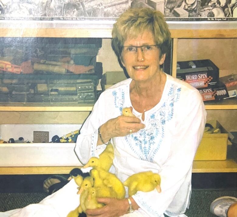 Marlene Mutch sits on the floor at Oakenwald School holding a bunch of ducklings. 