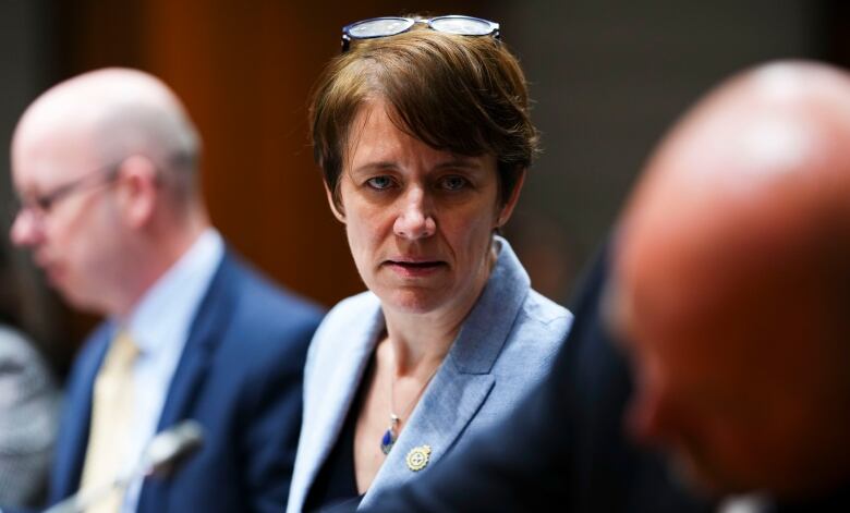 A woman in a blue suit jacket looks across the camera.