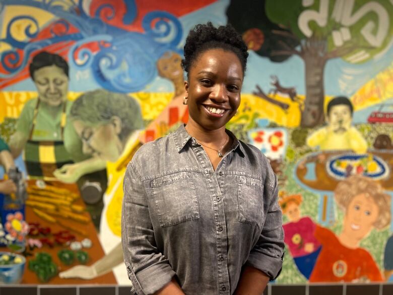 A woman smiles at the camera, with a mural behind her. 