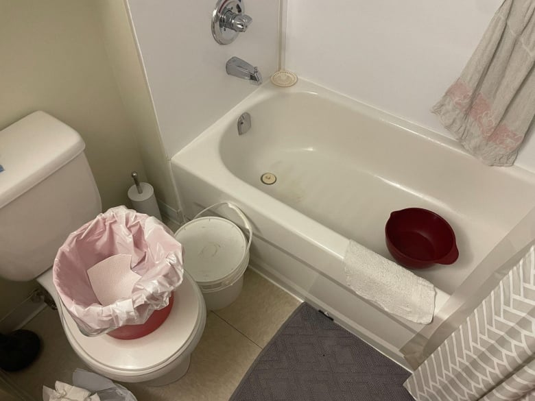 A buckets lined with a plastic bag sits on a toilet in a bathroom