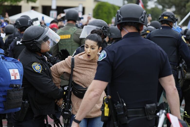 Police in helmets and face shields arrest a woman in a crowd.