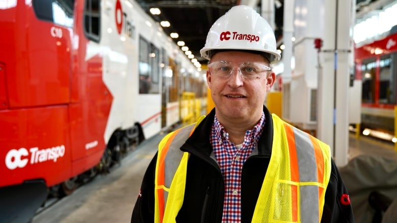 A man in a hard hat and a safety vest stands beside a red and white train